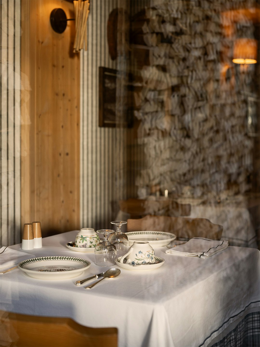 Tavola apparecchiata con tovaglia bianca e parete in pietra a vista, atmosfera rustica montana