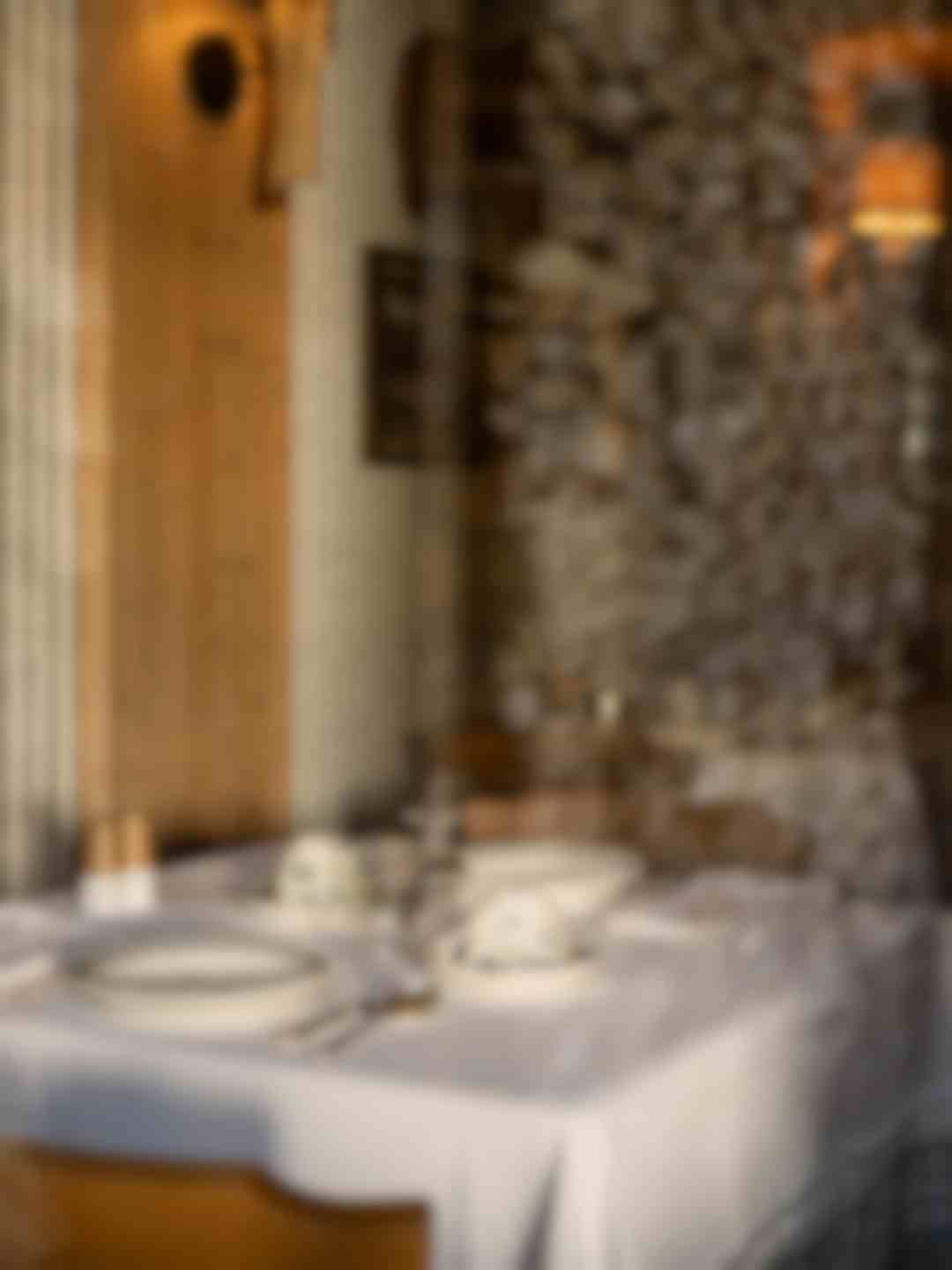 Tavola apparecchiata con tovaglia bianca e parete in pietra a vista, atmosfera rustica montana