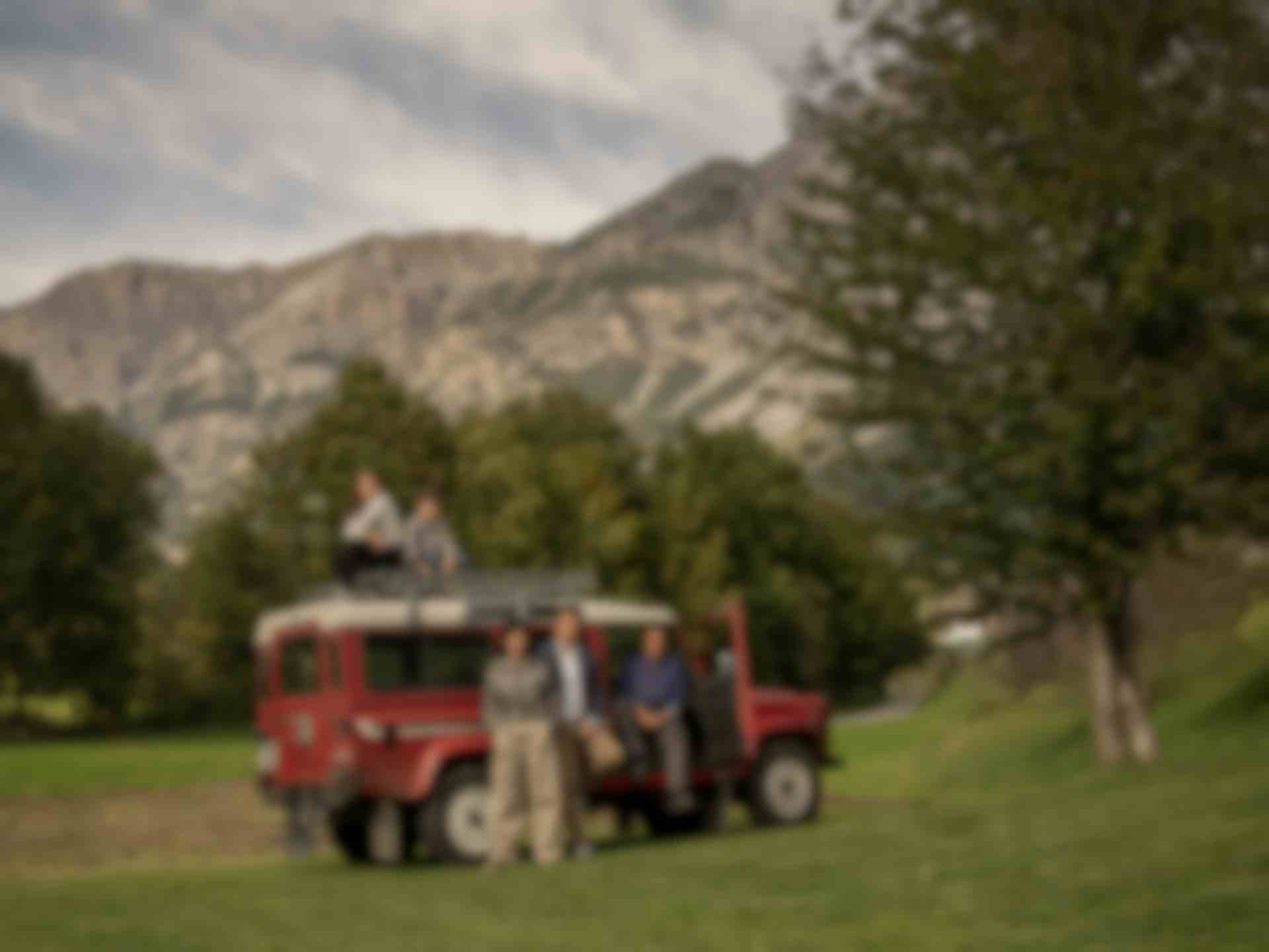 Foto di famiglia con Land Rover d'epoca rosso su prato alpino con vista sulle montagne