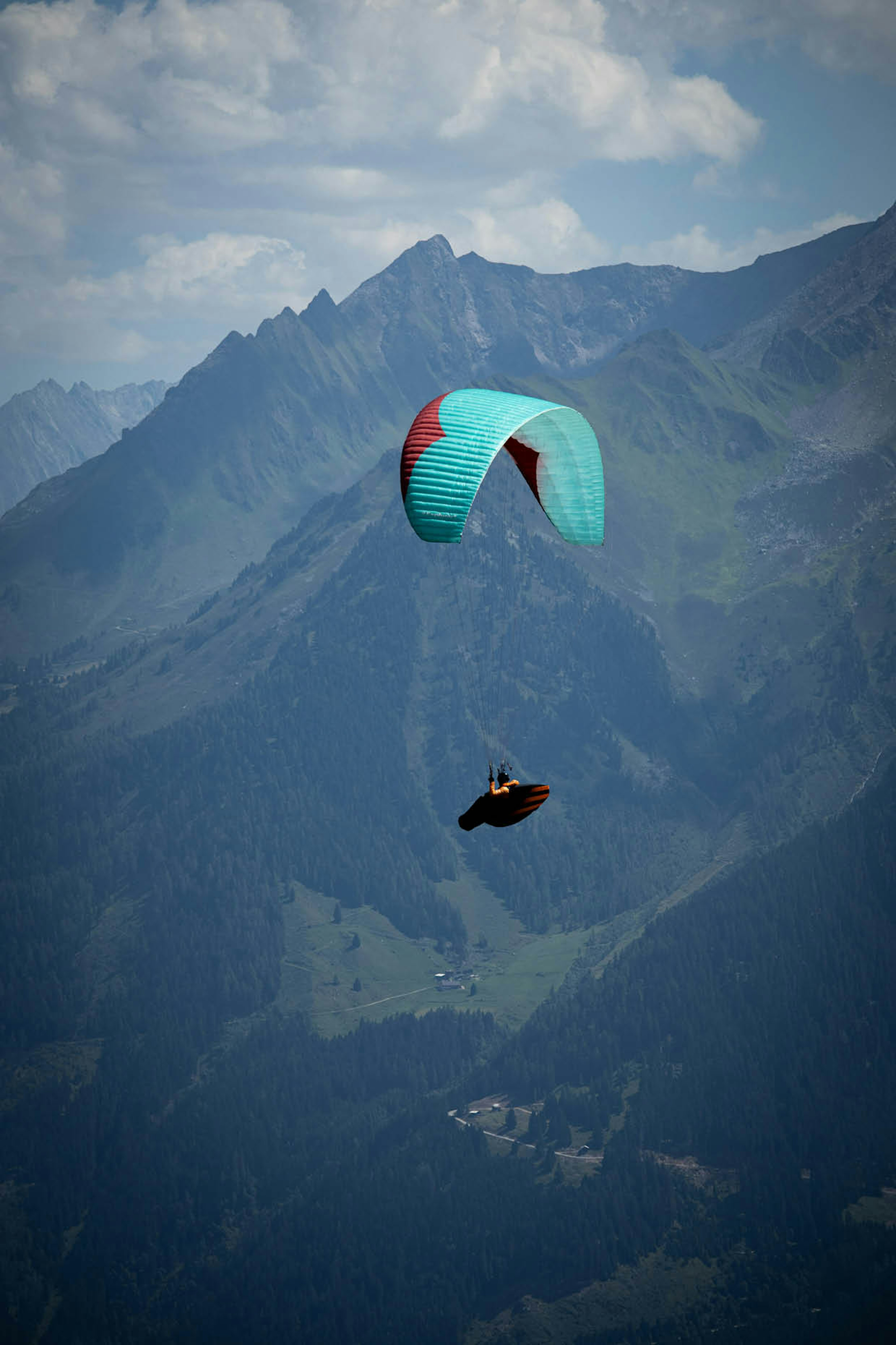 Parapendio con vela turchese in volo sopra le valli alpine, vista mozzafiato sulle montagne