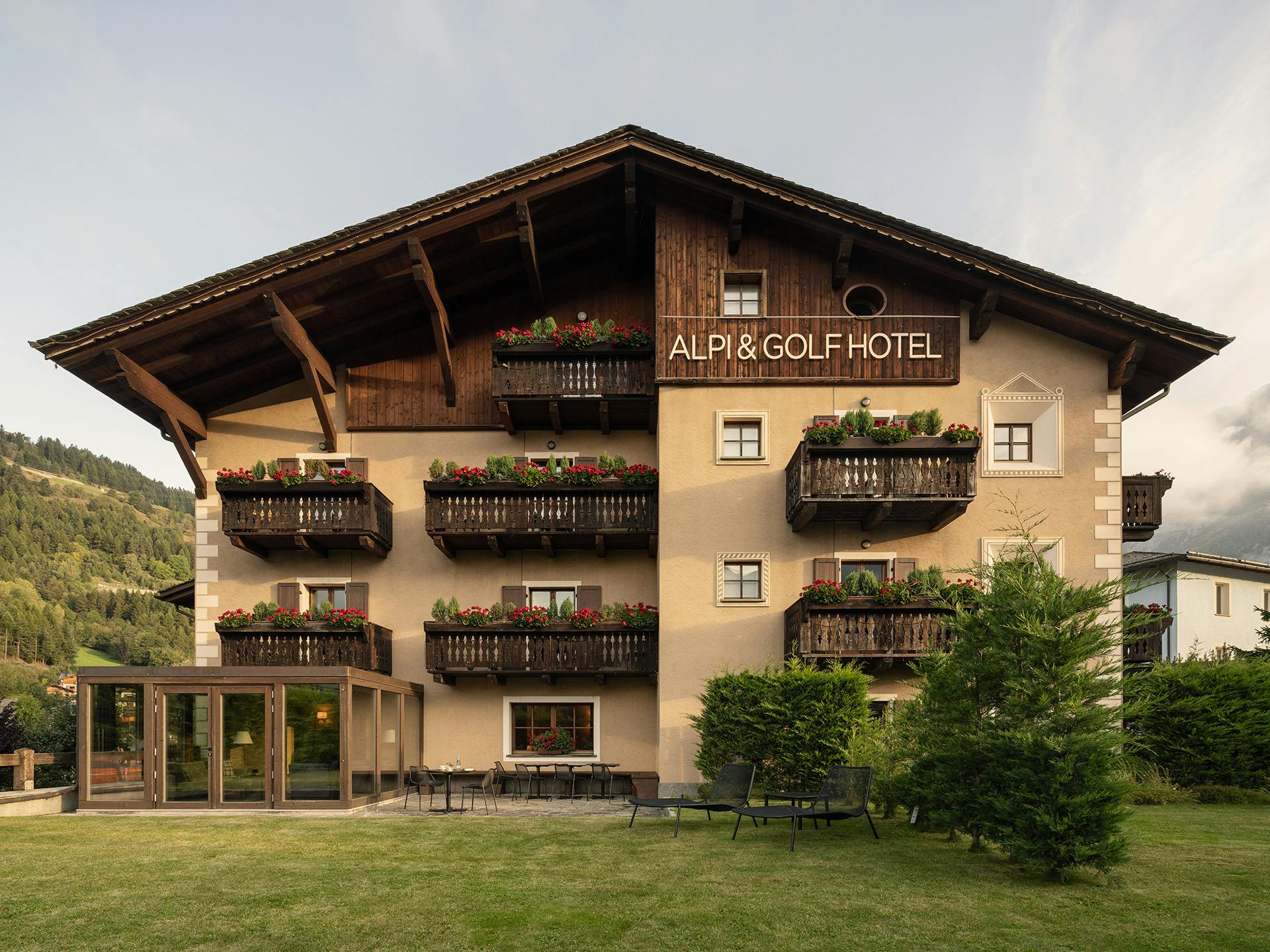 Alpi & Golf Hotel, struttura tradizionale alpina con balconi in legno fioriti, ampio giardino e vista sulle montagne