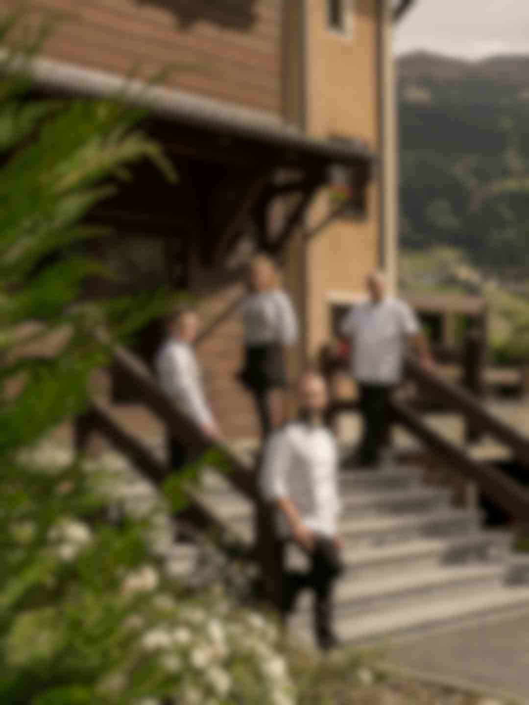 Staff dell'hotel in divisa elegante sulle scale d'ingresso in legno, panorama alpino sullo sfondo