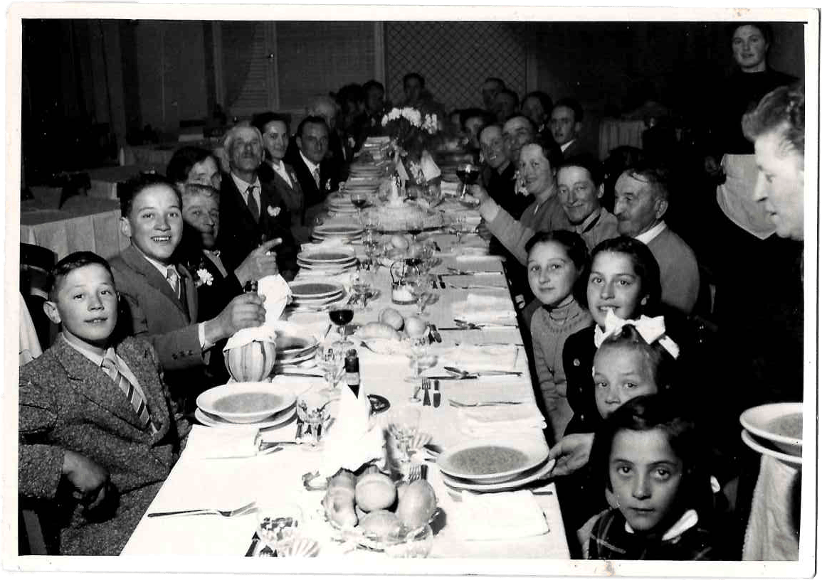 Grande banchetto familiare in bianco e nero con tavola apparecchiata, adulti e bambini riuniti per celebrazione
