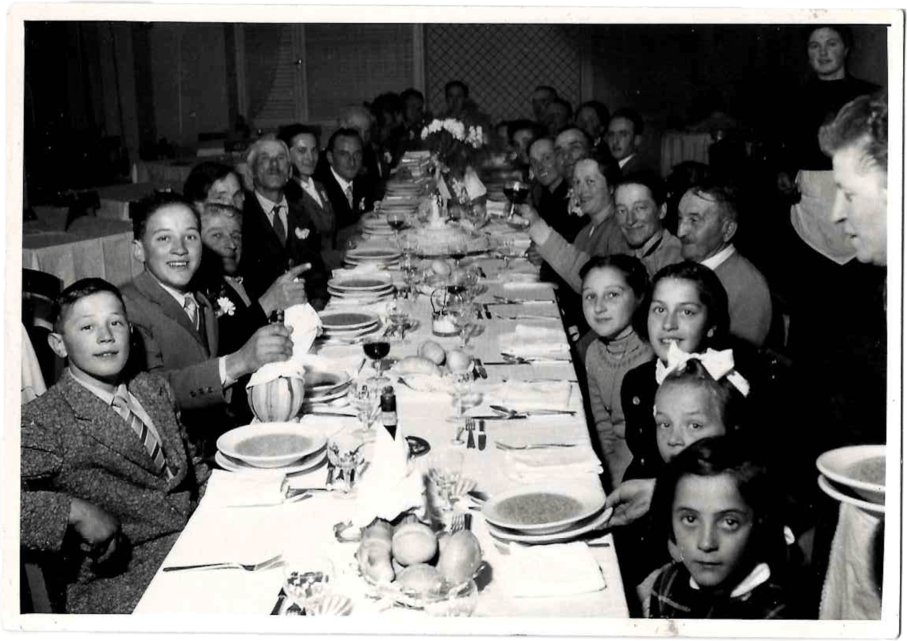 Grande banchetto familiare in bianco e nero con tavola apparecchiata, adulti e bambini riuniti per celebrazione