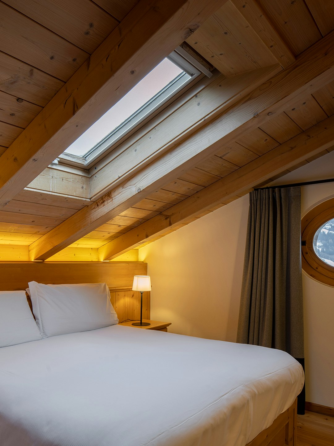 Letto matrimoniale sotto l'abbaino e oblò con vista montagna, parquet in legno di abete.