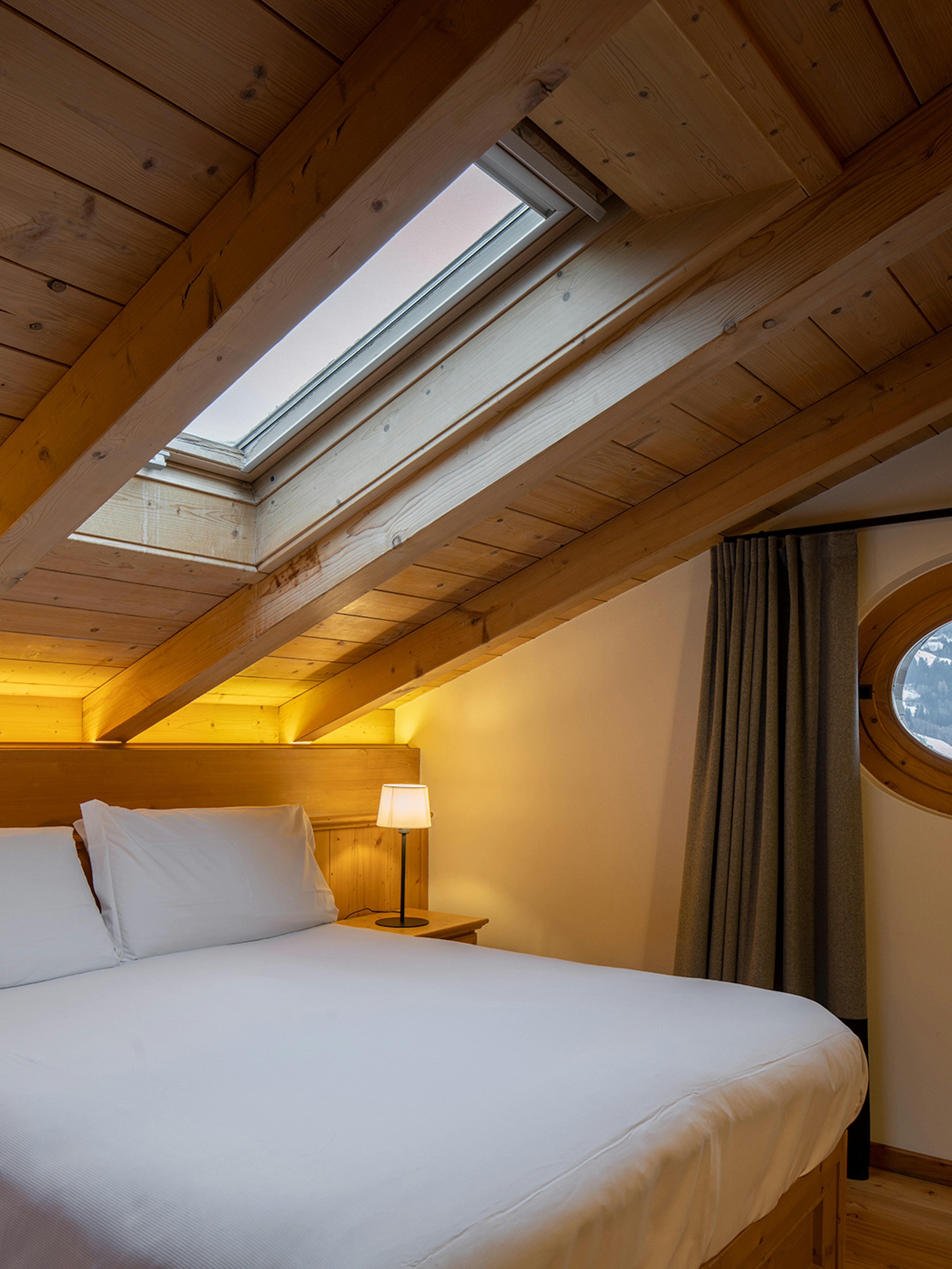 Letto matrimoniale sotto l'abbaino e oblò con vista montagna, parquet in legno di abete.