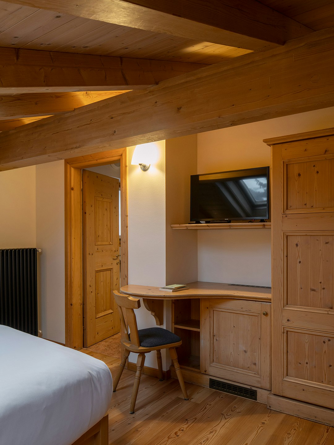 scrivania in legno con tv, travi e armadio in legno di abete, letto con lenzuola bianche.