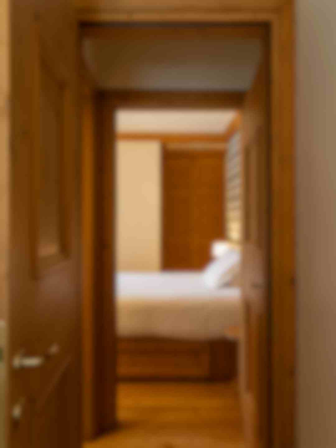 Porta aperta su camera da letto principale, letto matrimoniale con lenzuola bianche e doppi cuscini, porte e armadi in legno di abete.