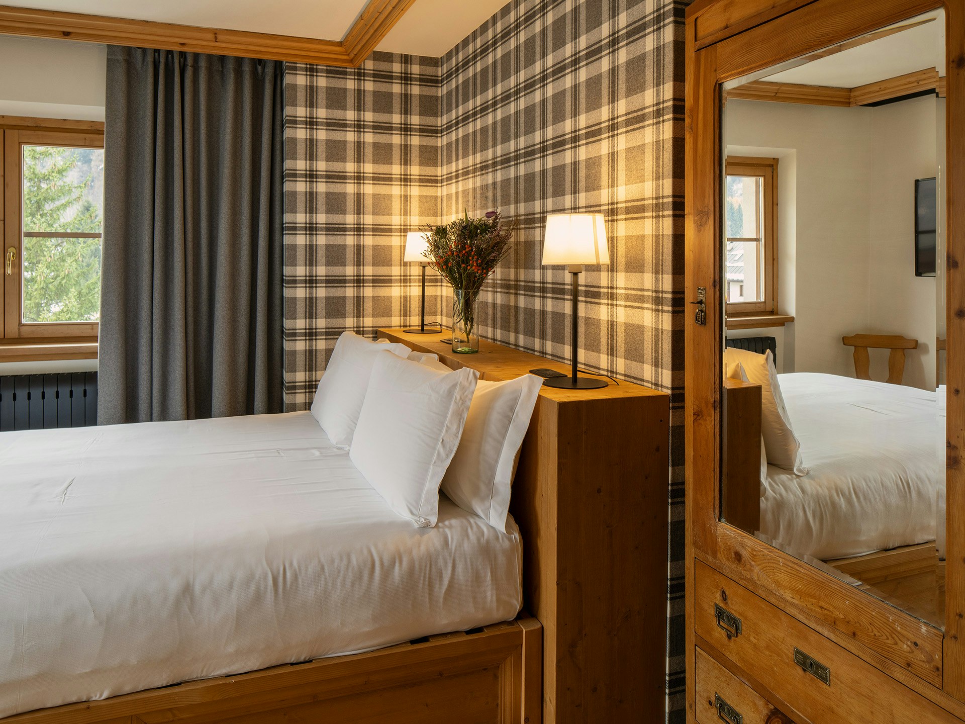 Stanza in legno con carta da parati in stile tartan, tenda di stoffa grigia e armadio antico con grande specchio.