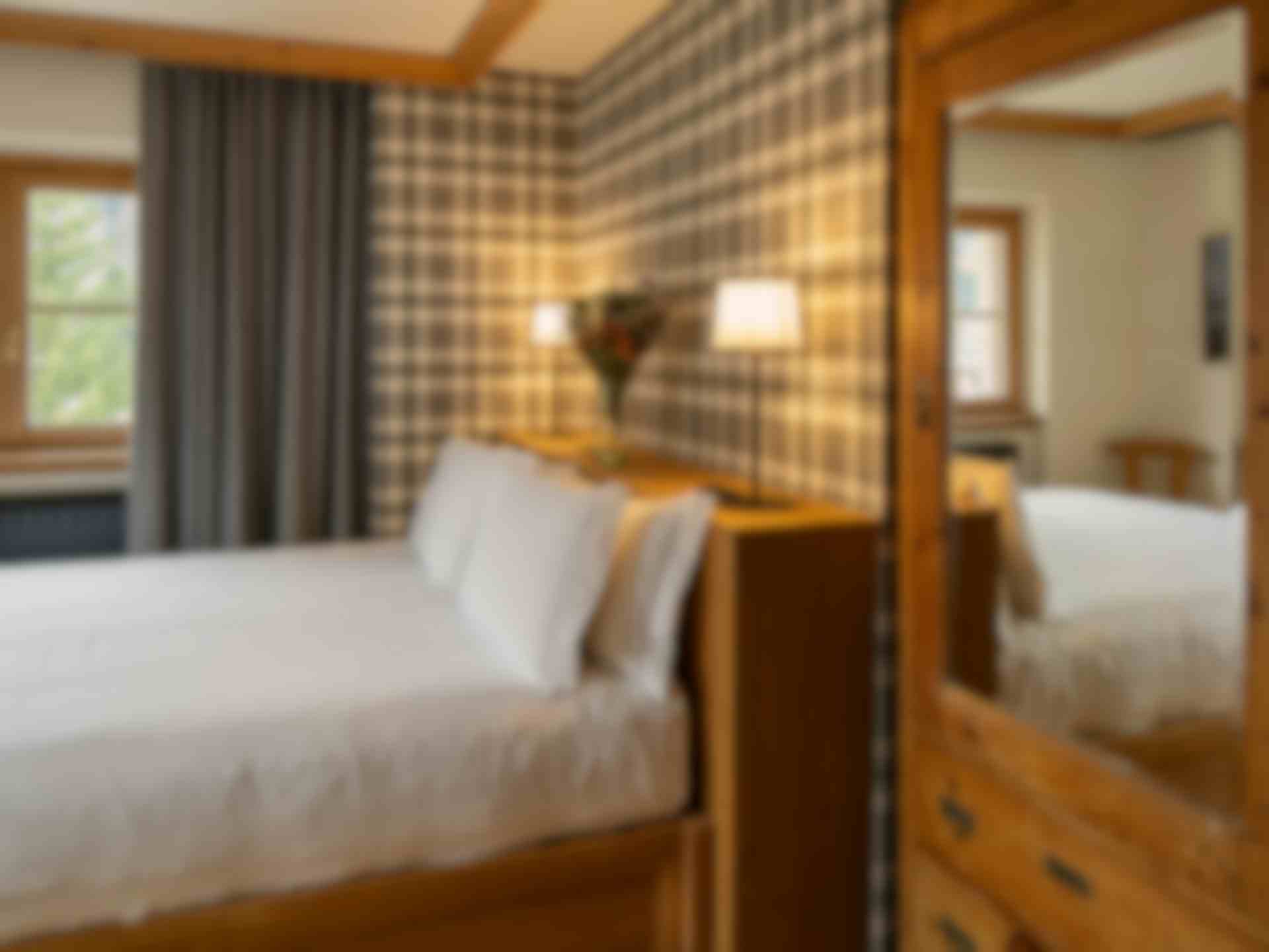 Stanza in legno con carta da parati in stile tartan, tenda di stoffa grigia e armadio antico con grande specchio.