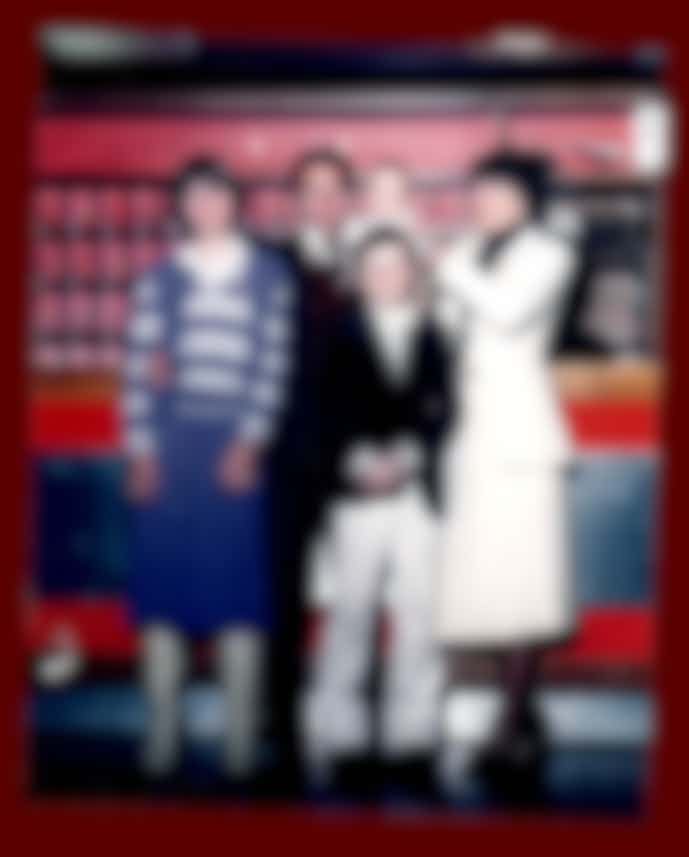 Famiglia con tre figli davanti alla reception dell'hotel, atmosfera anni '80 con arredamento rosso