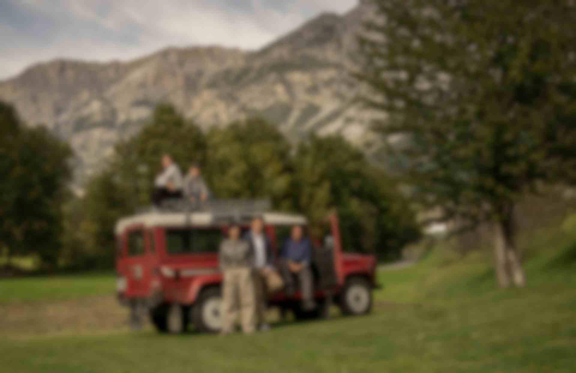Famiglia dell’Hotel Alpi & Golf a Bormio riunita accanto a una Land Rover rossa d’epoca, con le montagne alpine sullo sfondo e prati verdi intorno.
