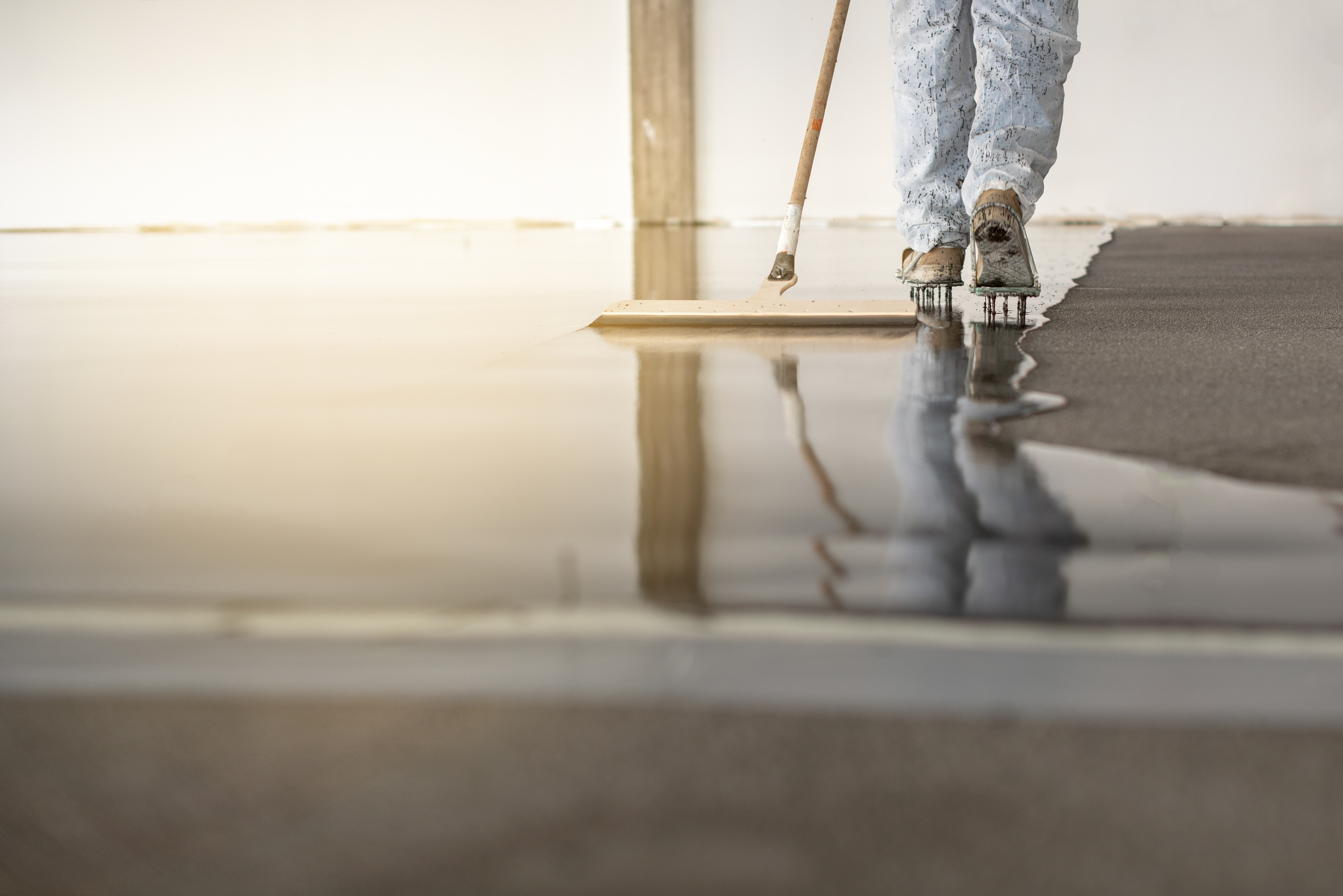 Applicator laying a seamless resin floor, wet finish reflecting the light.