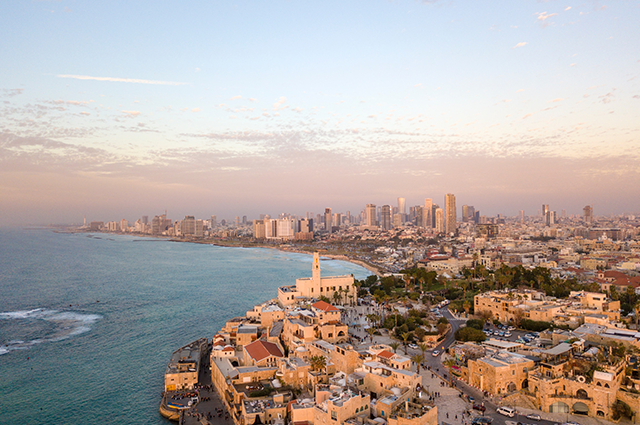 Tel Aviv skyline in the early evening with the sun casting a warm glow over the city. The traditional city sites by the sea with the modern and futuristic skyscrapers looming in the distance 