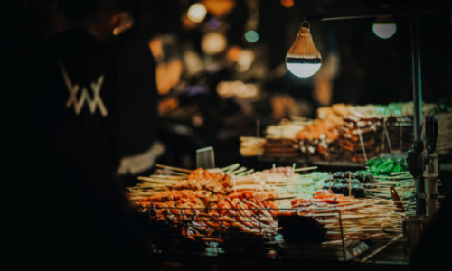 A photo of a street food stall taken at night, with lamplight highlighting skewered foods