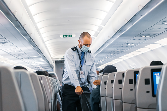 Flight Attendant collecting rubbish on a plane while wearing a face mask 