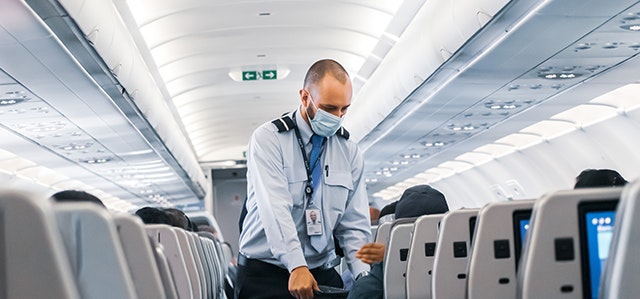 Flight Attendant collecting rubbish on a plane while wearing a face mask 