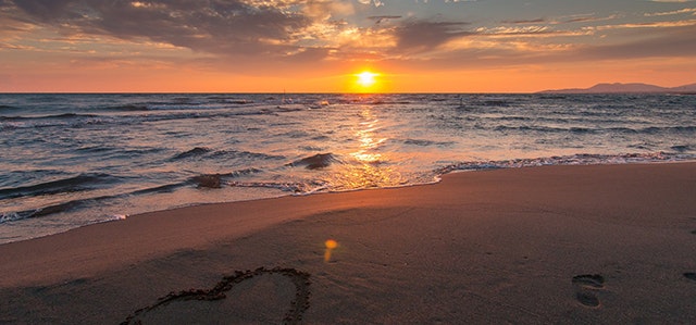 Love heart drawn in the sand of a beach with a setting sun