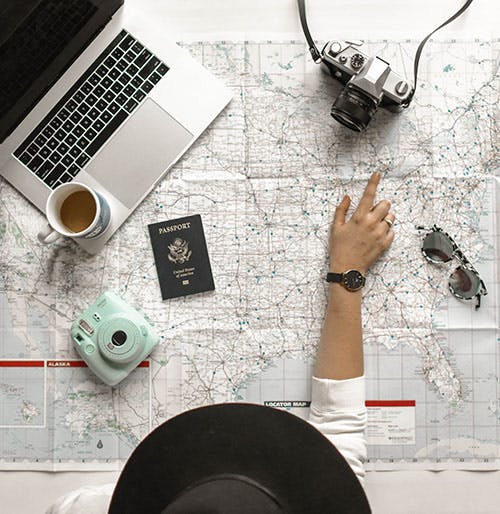 Picture of a map, passport, cameras, laptop and a person making travel plans