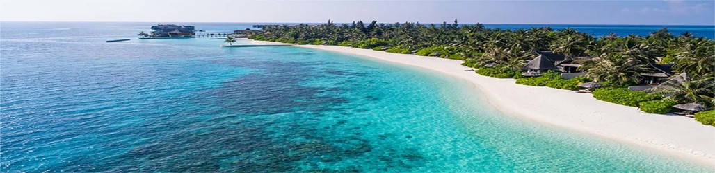 An inviting blue sea runs along the paper white sand beach with luxurious huts and green palms 