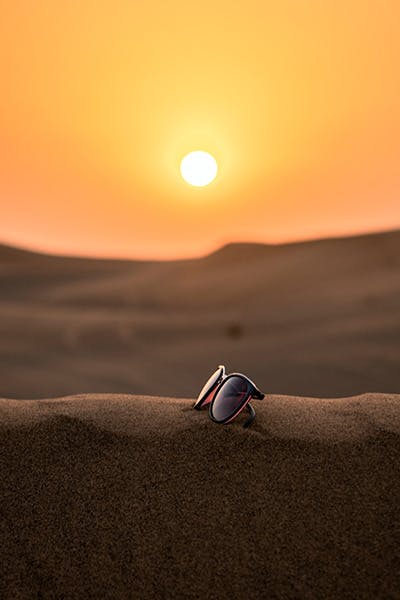 Picture of sunglasses on the sand with sunset in the background