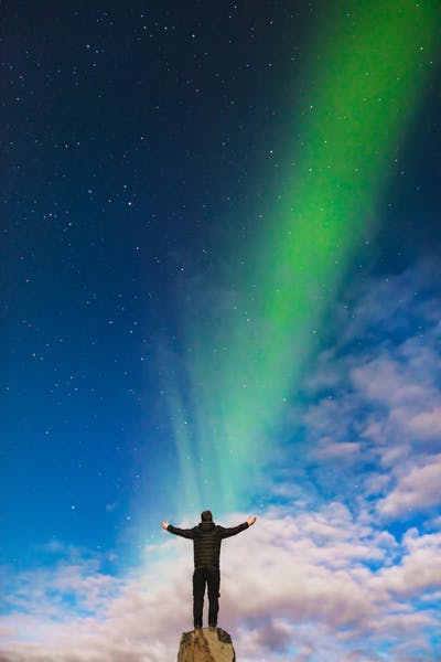A man standing on a rock in front of the Northern lights