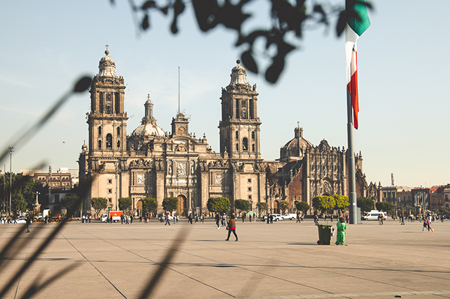 A stone cathedral in Mexico City with the Mexican flag to the right