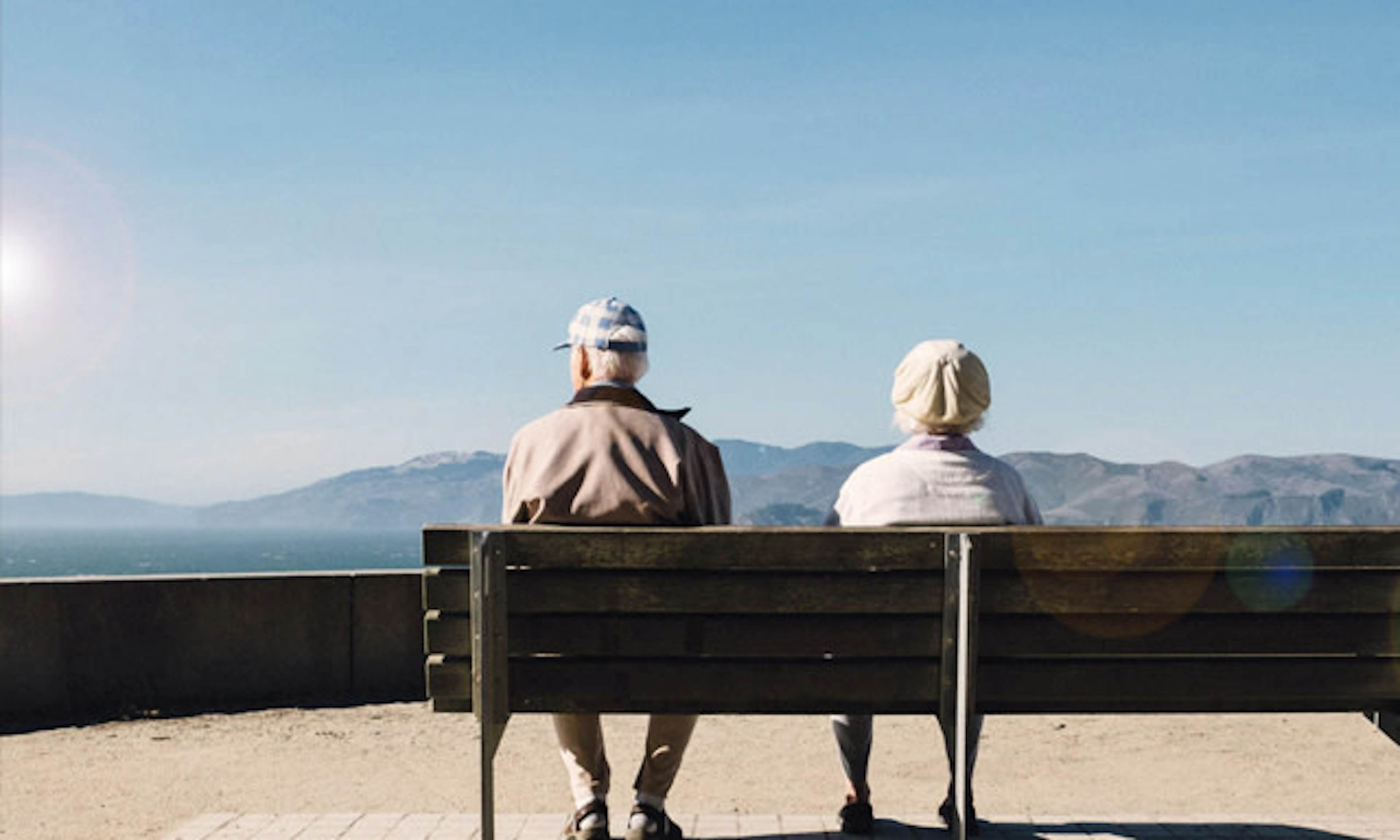 2 senior citizens sat on a bench looking out to sea