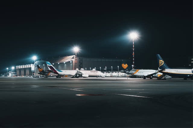 The concourse of an airport at night being illuminated by overhead lights shining on the Thomas Cook, Ryanair and Eurowings aircraft below 