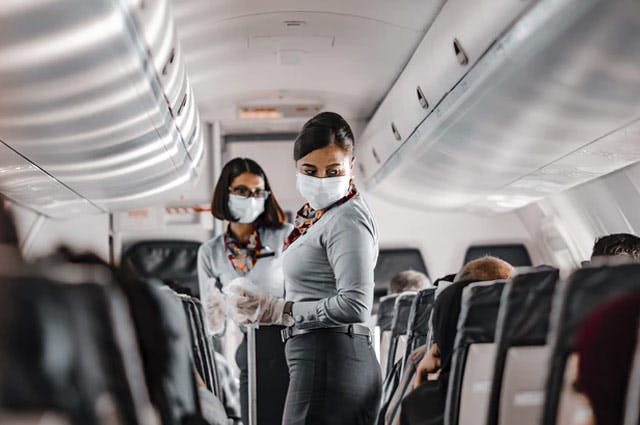 View down the aisle of a plane with flight attendants wearing COVID face coverings