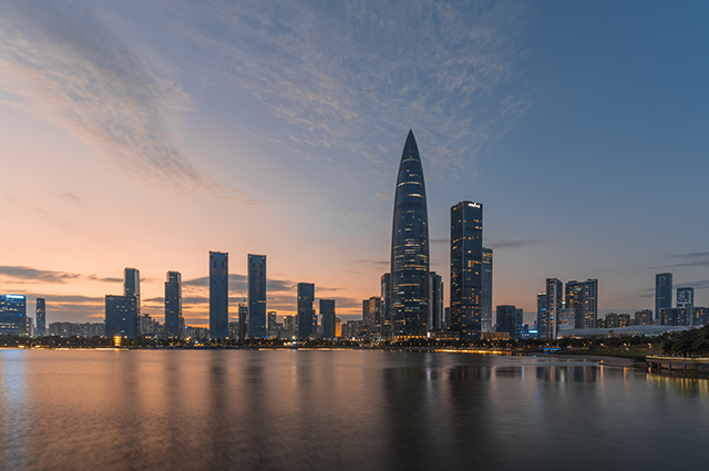 The futuristic skyline of Shenzhen bathed in dim glow from the setting sun casting reflections over the water below
