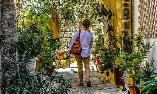Woman wearing sandals walking through a small street somewhere hot, with warm light and potted plants