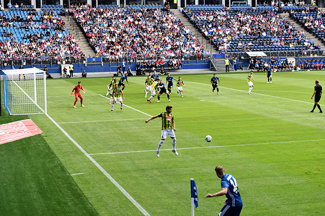 Football match being played on a grass pitch with crowds of fans sitting around the pitch