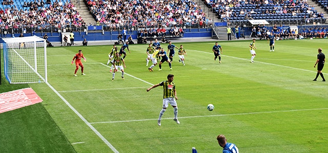 Football match being played on a grass pitch with crowds of fans sitting around the pitch