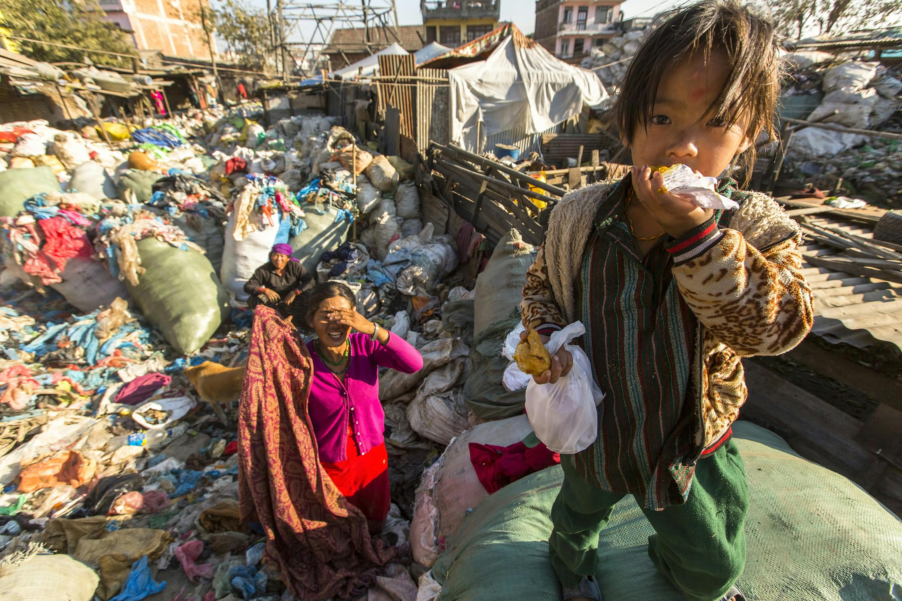 Child living in extreme poverty eating a morsel in a heavily-polluted town