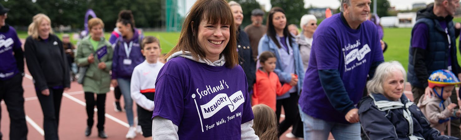 Lady smiling within in crowd wearing a AlzScot Memory Walk t-shirt