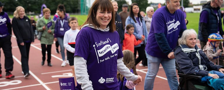 Lady smiling within in crowd wearing a AlzScot Memory Walk t-shirt