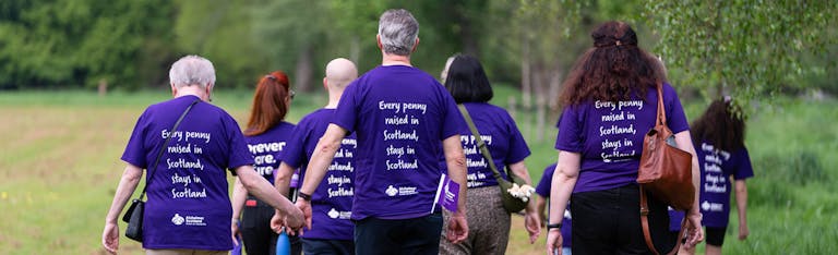 A group of people walking away from the camera, all wearing Alzheimer Scotland t-shirts. The message on the back of each shirt reads: 'Every penny raised in Scotland stays in Scotland.'