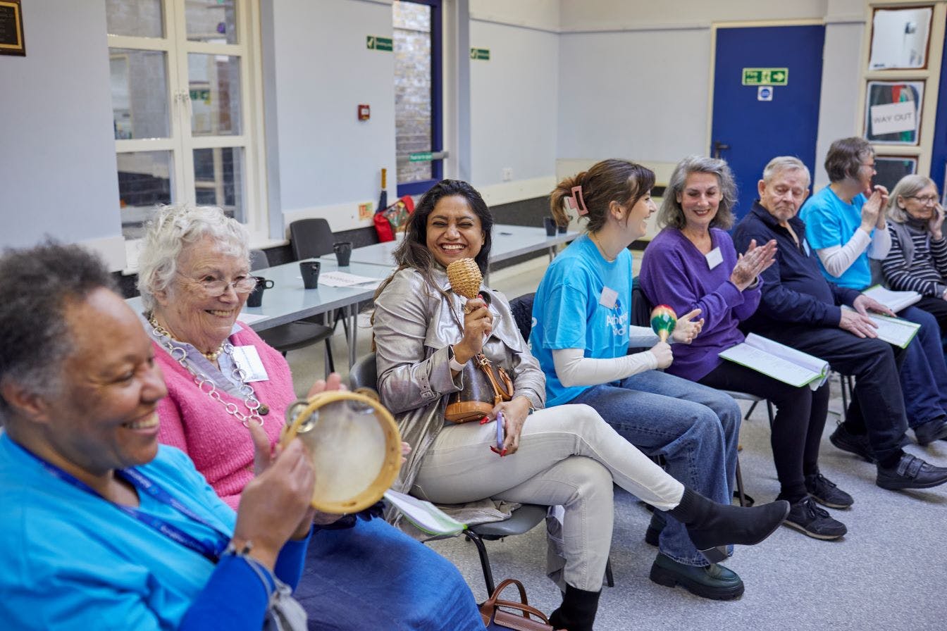 Group of people seated and smiling, with musical instruments in their hands.