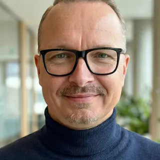 Professional portrait headshot of Thomas Schroepfer, Go-to-Market Program Manager at amazee.io, set against a soft, blurred office background, featured on the team section for the DrupalCon Rotterdam landing page.