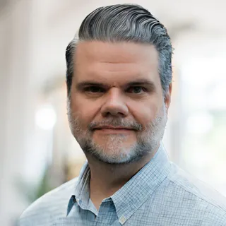 Professional portrait headshot of Hank VanZile, Senior Director Customer Experience at Tag1, set against a soft, blurred office background, featured on the team section for the DrupalCon Rotterdam landing page.