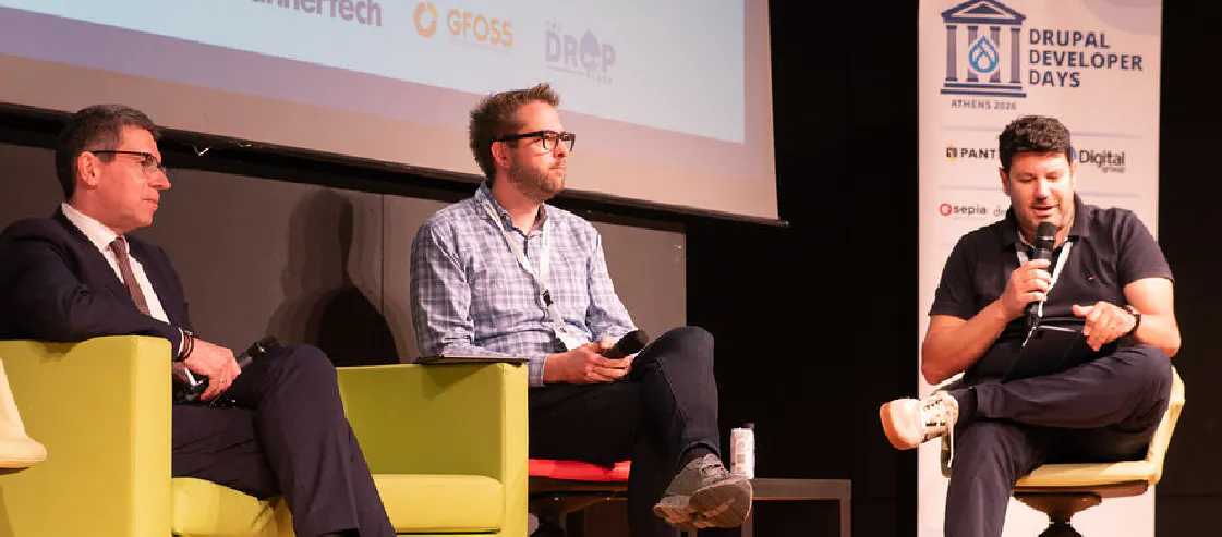 A panel discussion at Drupal Developer Days Athens 2026. Three men are seated on stage in lime green and yellow chairs, with one man speaking into a microphone. A large banner with the event logo and sponsor names stands to the right, and a presentation screen with organization logos is visible in the background.