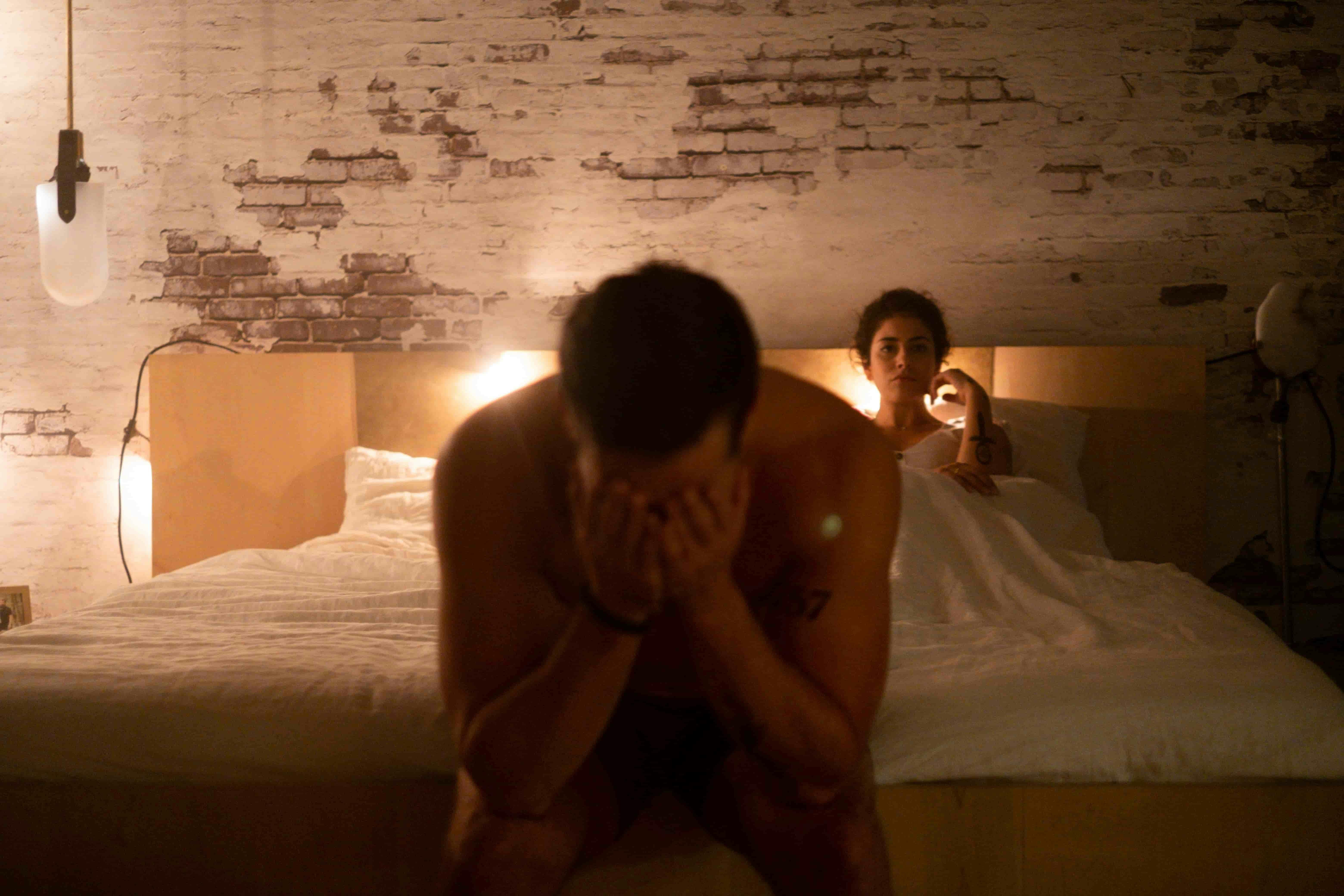 Man sat on the end of a bed with his head in his hands