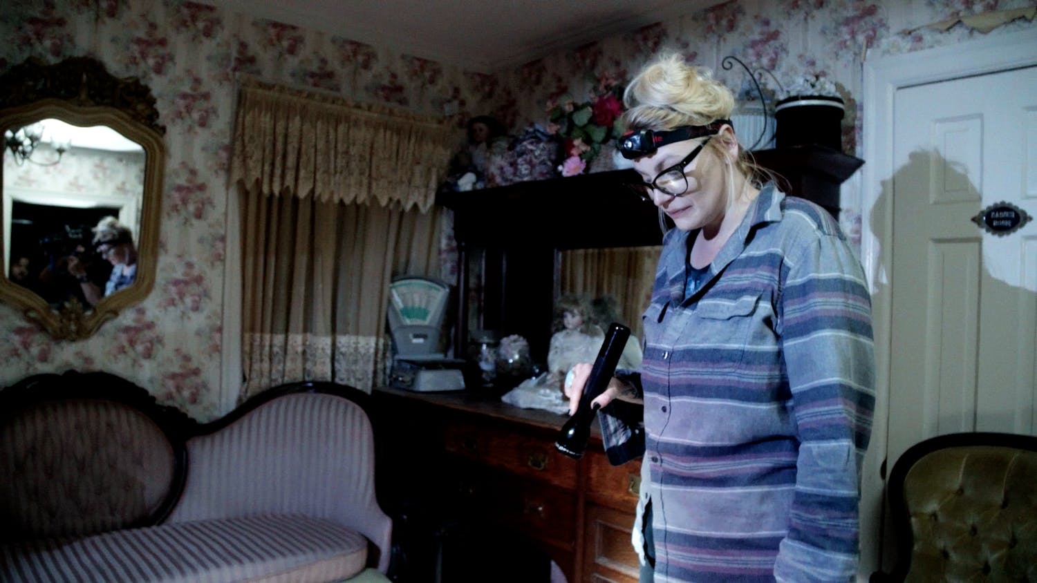 Woman in old house with torch on her head looking down