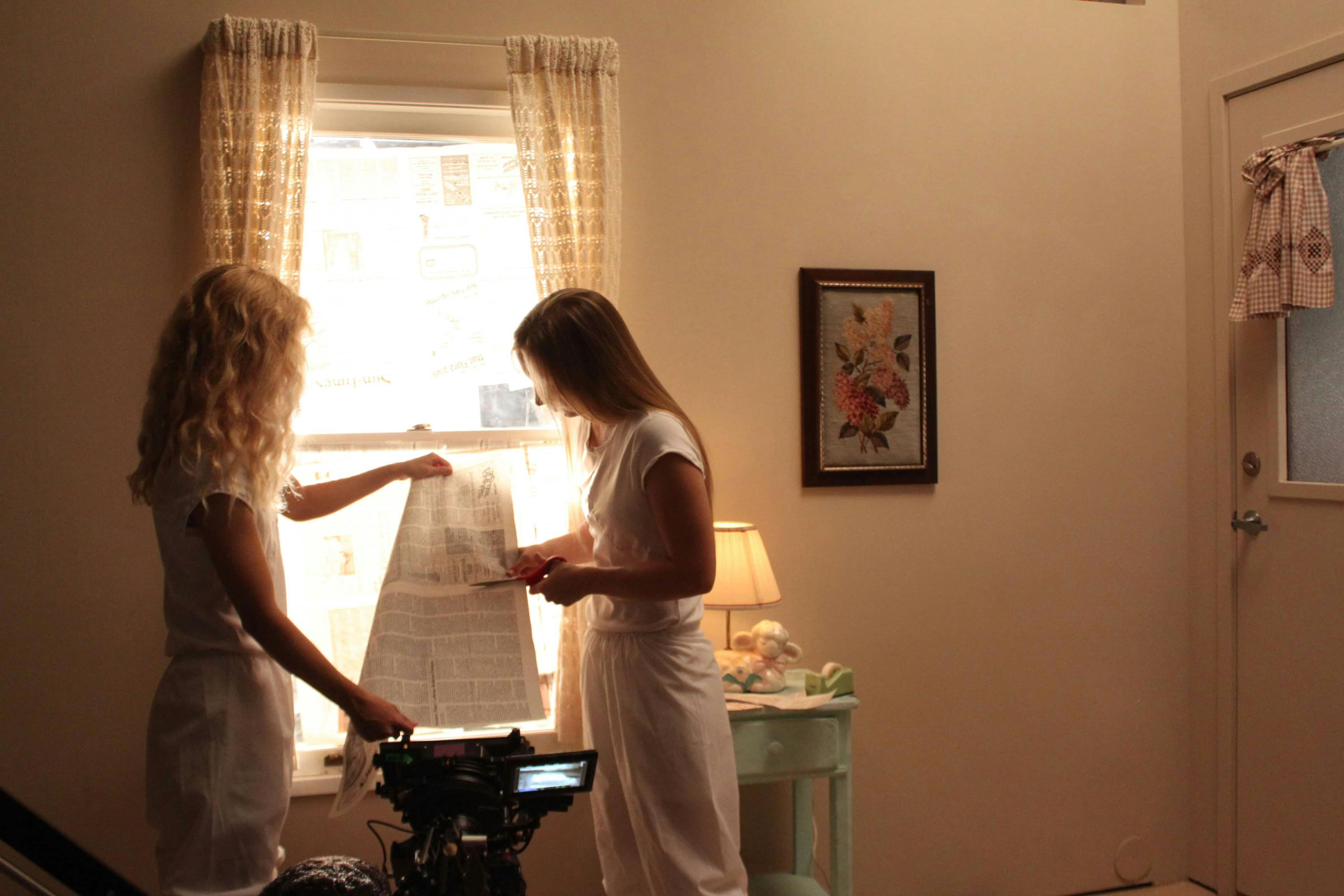 Two girls reading a paper by the window