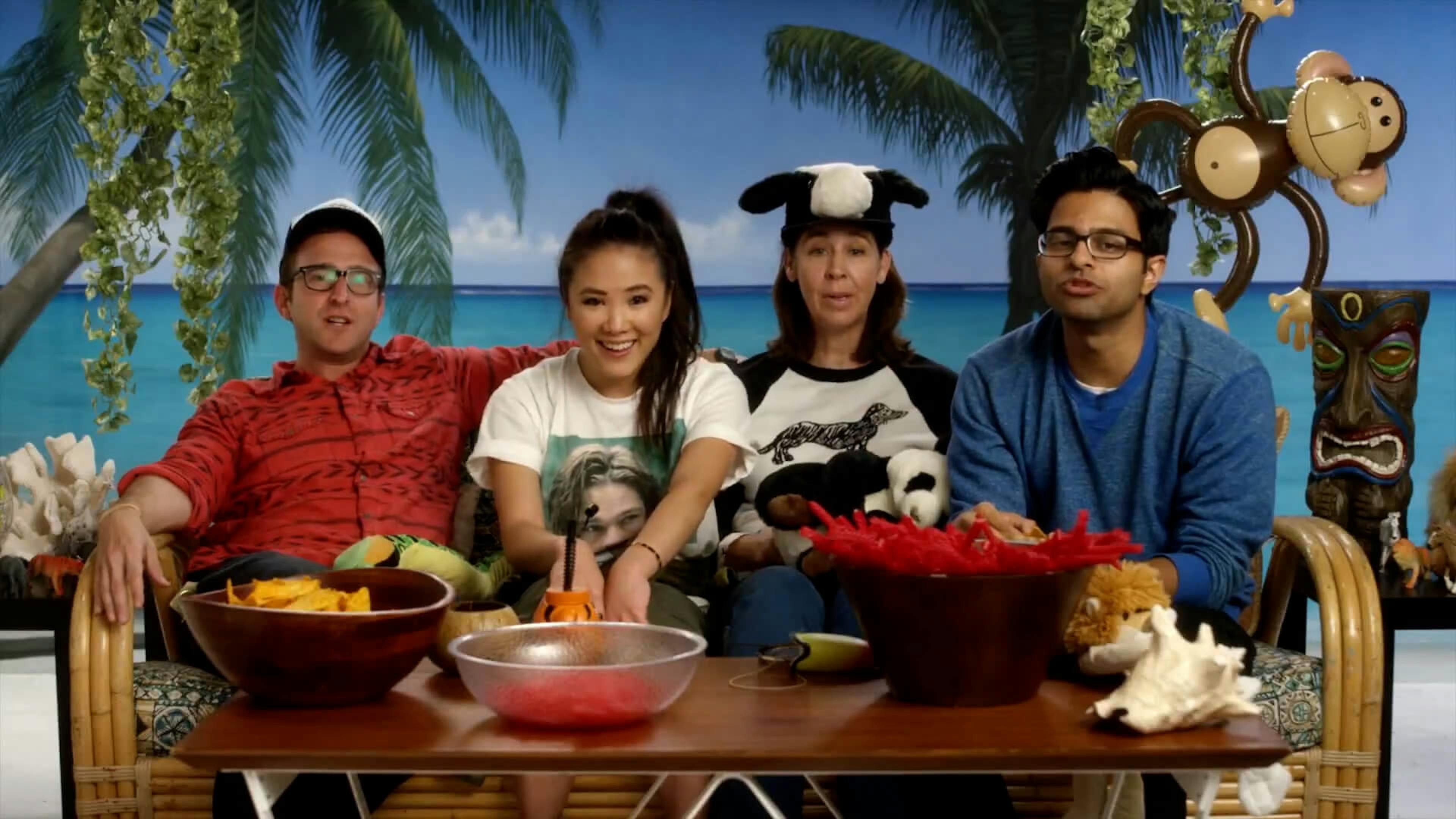 4 people sat on sofa in front of beach backdrop eating snacks
