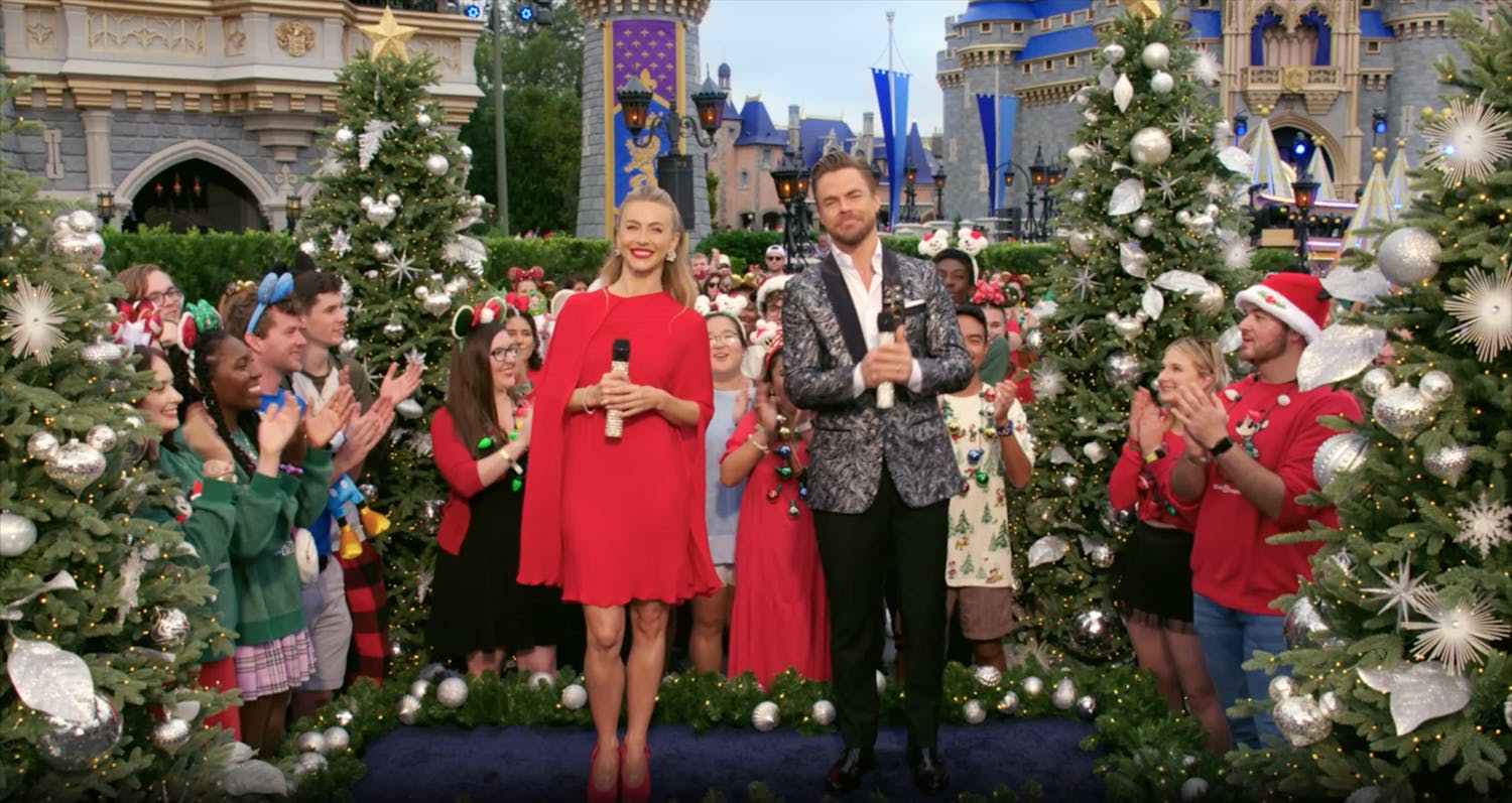 Two people stood on stage surrounded by people and Christmas trees