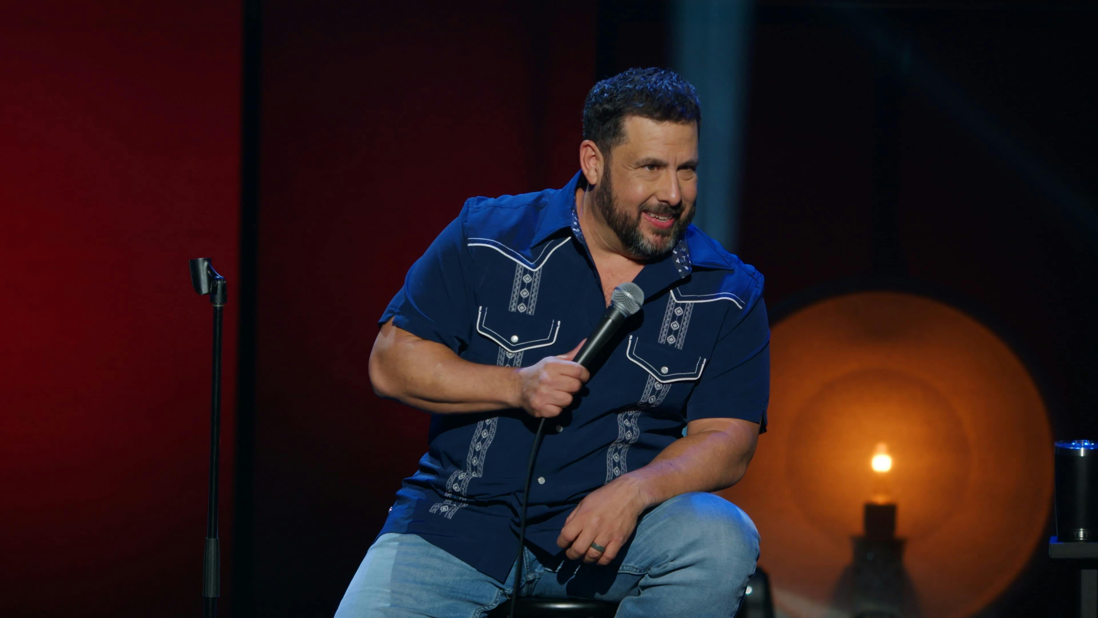 Man sat on chair on stage doing comedy routine