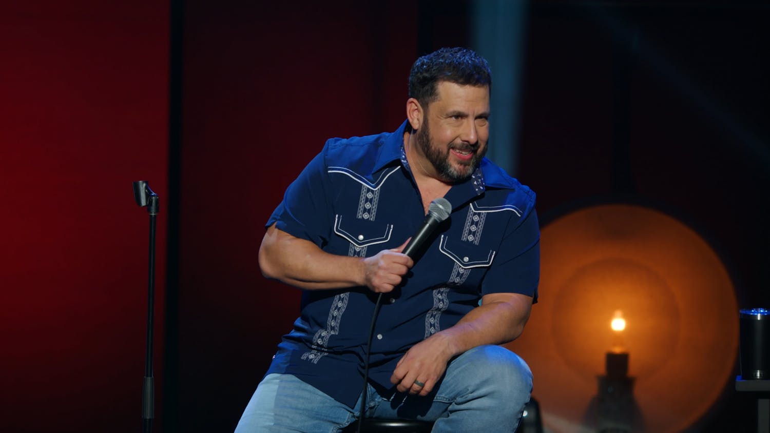 Man sat on chair on stage doing comedy routine