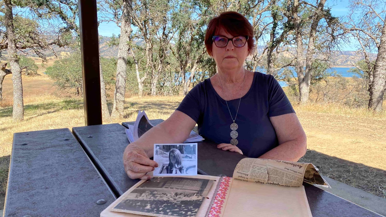 Woman sat at a table holding up a photo of a girl